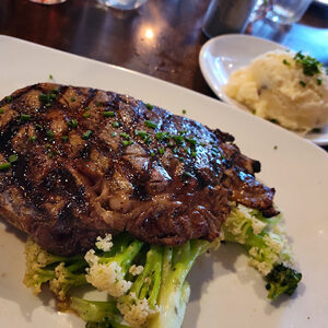 thick steak on plate over brocolli with mashed potato side dish